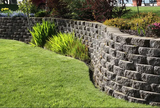 Curving stone-block retaining wall beside a garden lawn and planted border